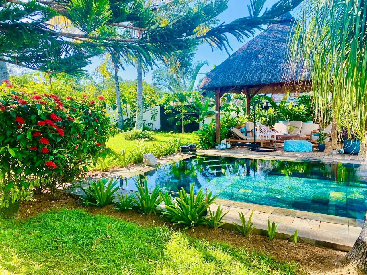 Tropical garden with a natural stone pool and a thatched pavilion